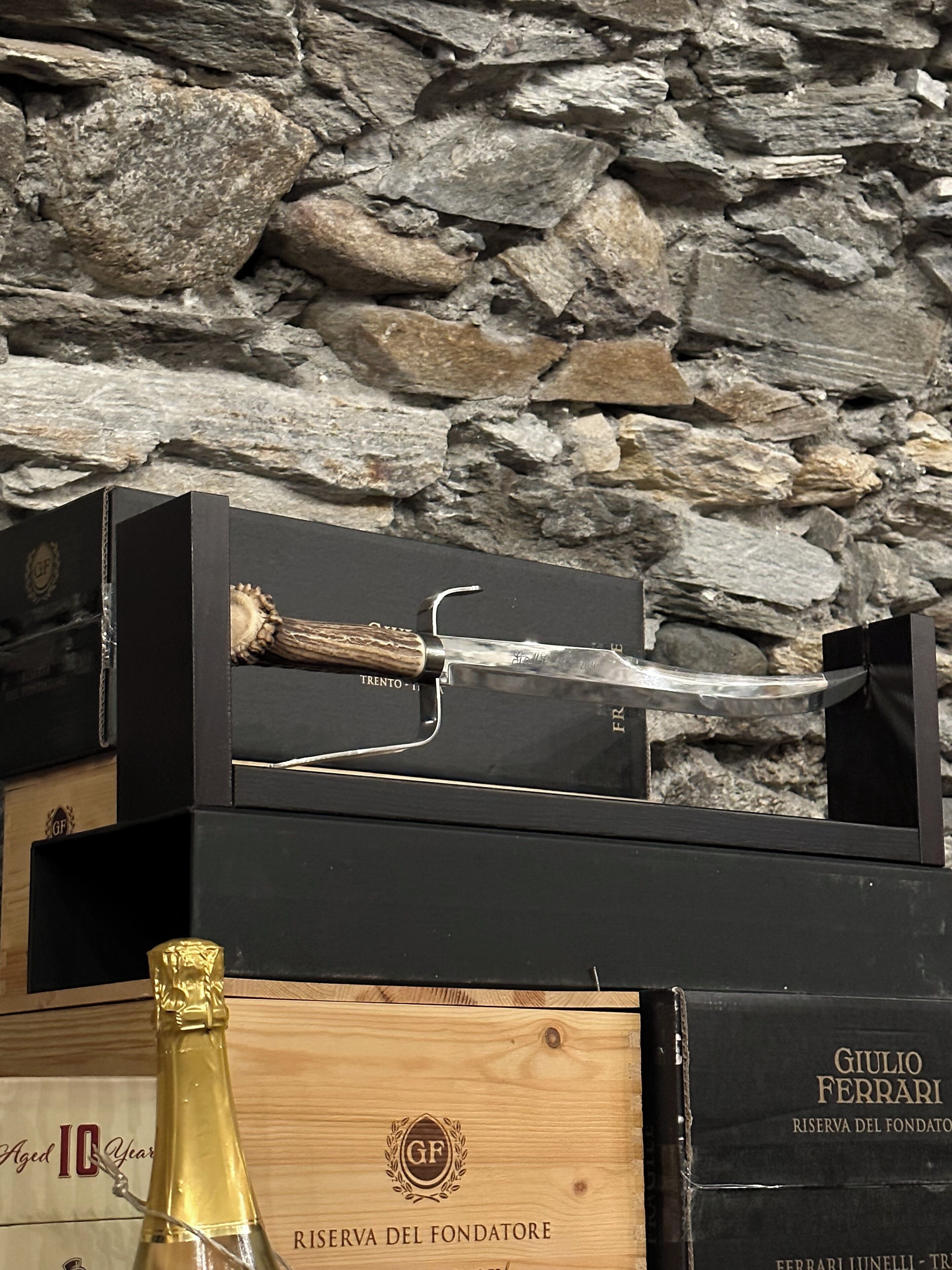 Une caisse en bois étiquetée « Giulio Ferrari Riserva del Fondatore », contenant une bouteille de champagne et un couteau posé sur le dessus.