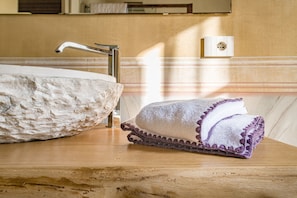 A bathroom with a large, textured basin and a rolled towel with purple trim. - VILLA CHIOVENDA Residenza d'Epoca (Premosello Chiovenda)