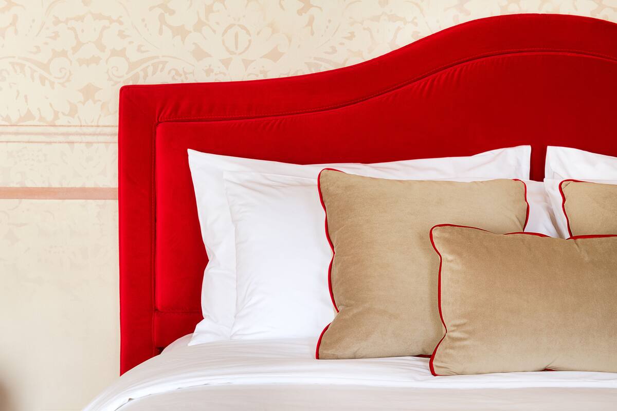Un lit avec une tête de lit rouge, des oreillers blancs et beige, et un mur à motifs en arrière-plan.