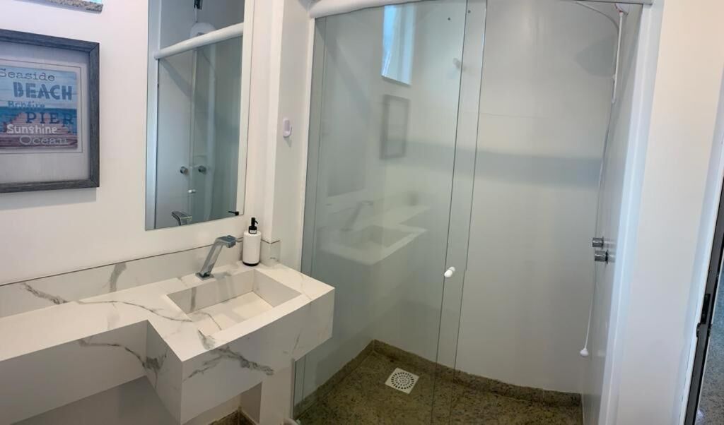 Une salle de bain avec un lavabo en marbre, une cabine de douche en verre et un panneau encadré accroché au mur.
