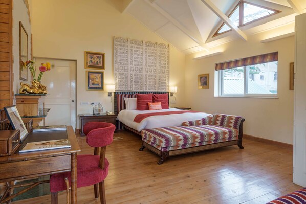 A bedroom with a large bed, a desk with a chair, a window with curtains, and a skylight.