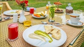 Un montaje para comer al aire libre con una mesa dispuesta para el desayuno, incluyendo platos de comida, bebidas y un jarrón con flores.
