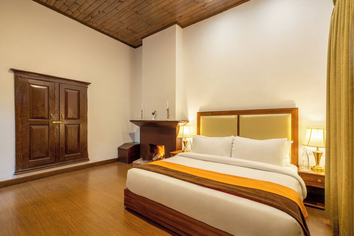 A hotel room with a large bed, wooden wardrobe, and a fireplace.