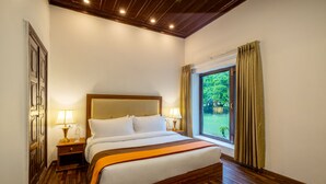 Una habitación de hotel con piso de madera, una cama grande con sábanas blancas, dos lámparas de noche y una ventana con cortinas.