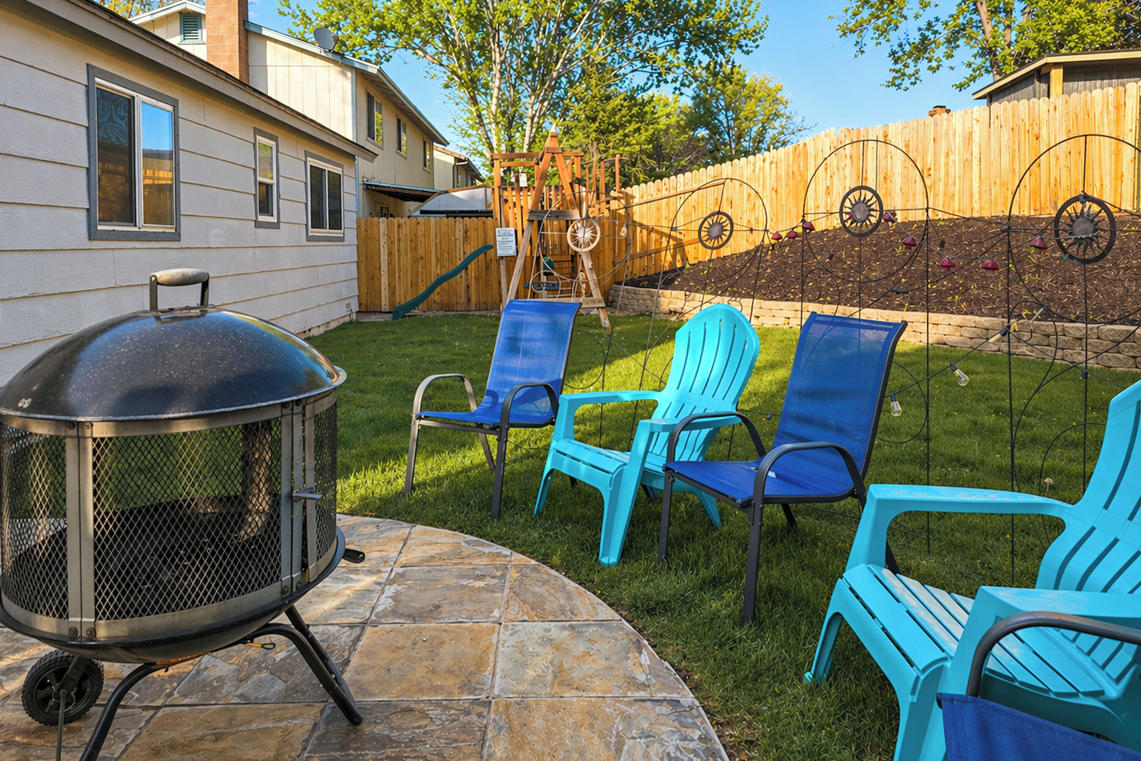 A backyard with a barbecue grill, outdoor chairs, and a wooden fence.