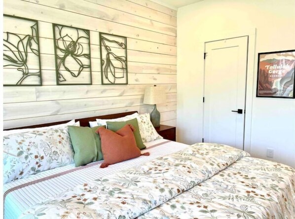 A bedroom with a wooden headboard, floral bedding, and wall art.
