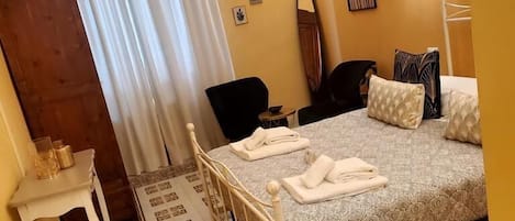 Un dormitorio con una cama, una silla, una mesita con un vaso y una botella, y una puerta.