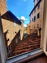 Una stretta via con tetti in tegole di terracotta ed edifici in pietra, vista da una finestra.