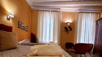 A hotel room with a bed, a chair, a table, and a window with curtains.