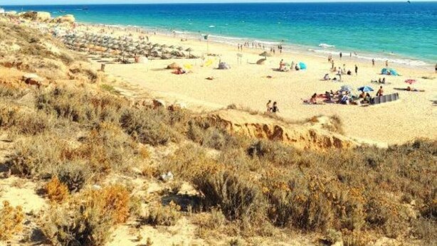 Een strand met mensen en parasols, zand en een heldere lucht.