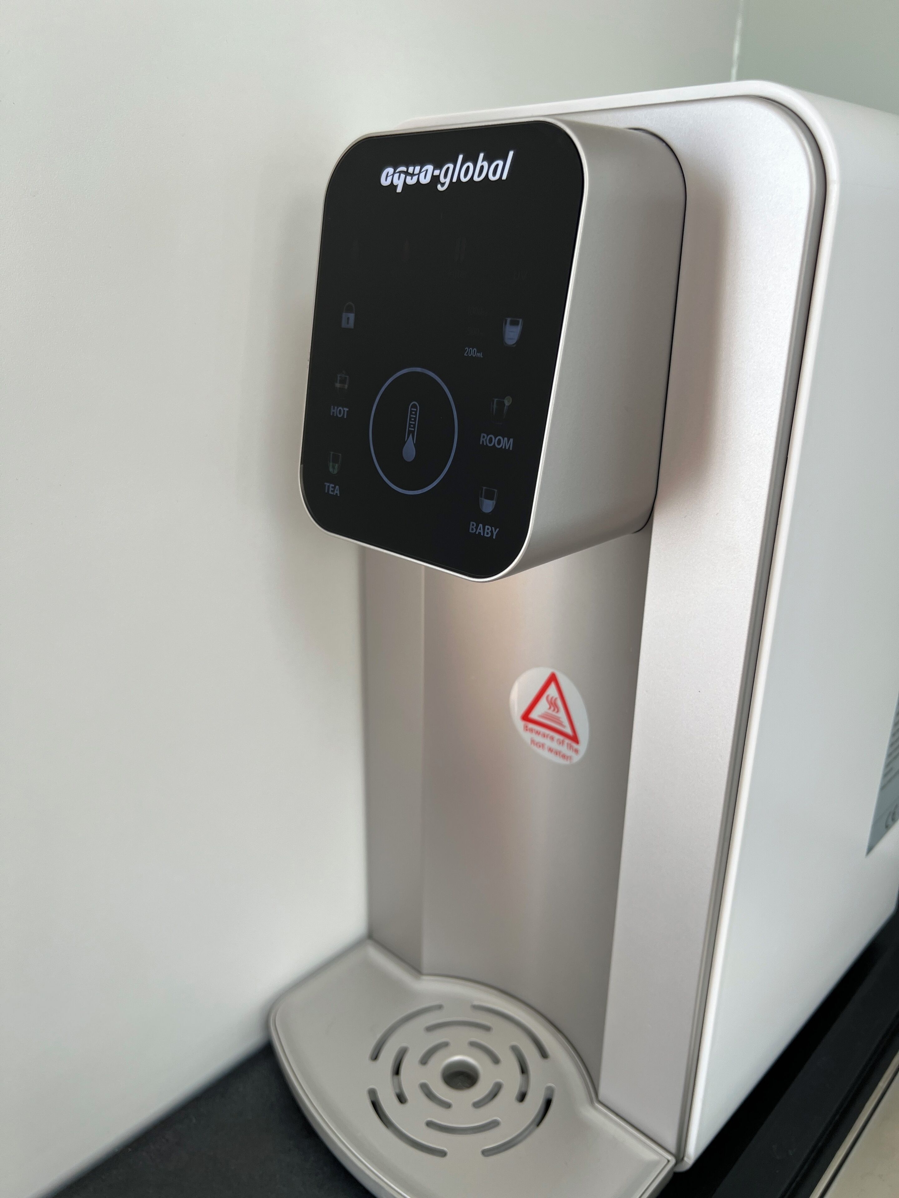 A water dispenser with a digital interface, a warning label, and a metallic finish.