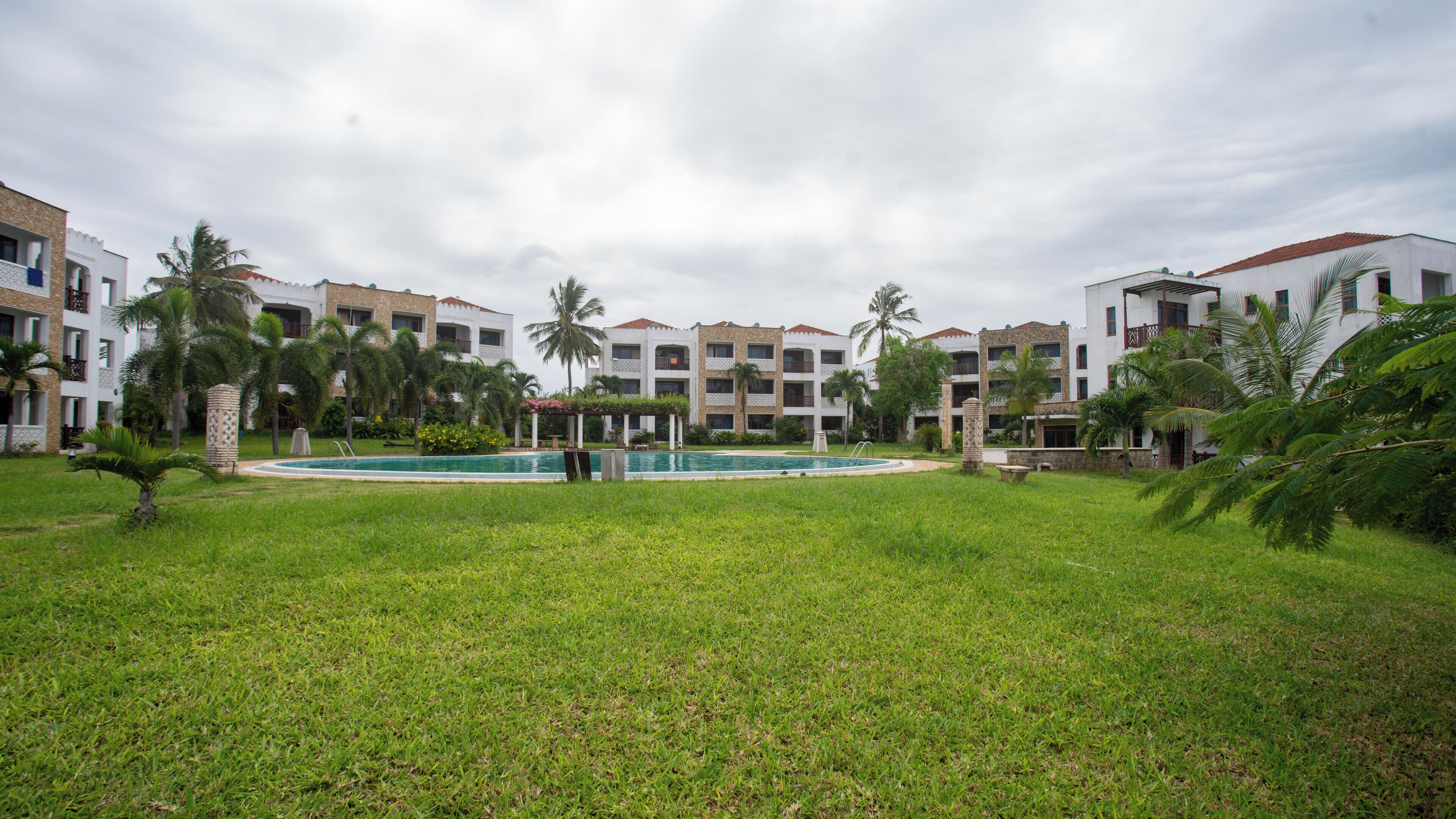 A hotel with a swimming pool, surrounded by lush greenery and palm trees.