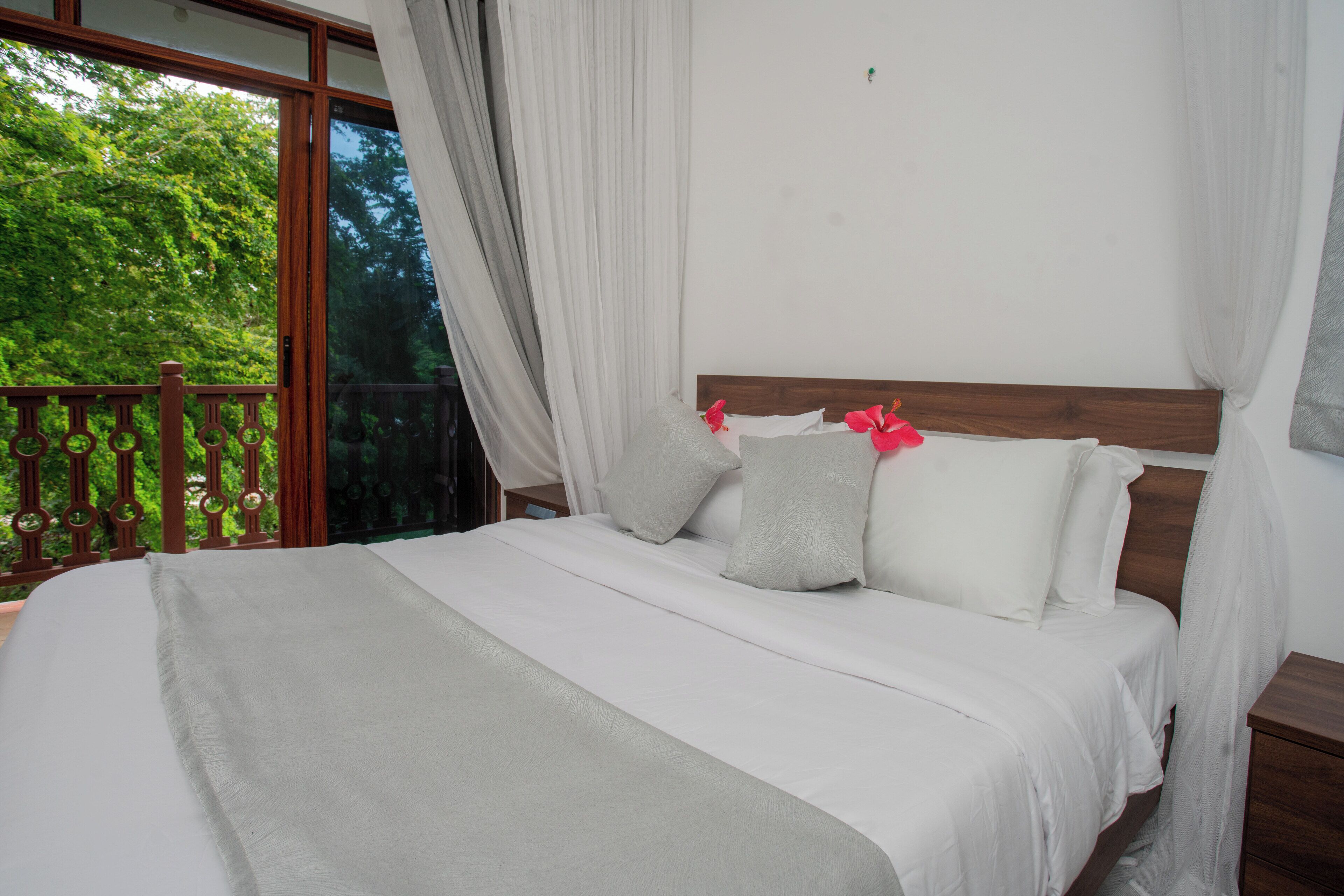 A bed with white bedding and a wooden headboard, a wooden nightstand, and a balcony with a wooden railing.