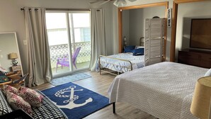 A hotel room with a bed, a desk with a lamp, a chair, a balcony with a view, and a sign indicating a guest dock. - Enjoy a Boathouse on the Bay in the heart of Downtown Sandusky.  (Sandusky)