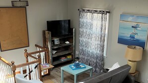 A living room with a grey sofa, a white armchair, a wooden entertainment unit, and a patterned curtain. - Enjoy a Boathouse on the Bay in the heart of Downtown Sandusky.  (Sandusky)