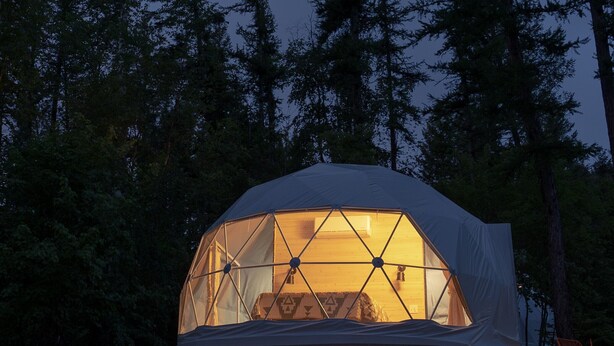A geodesic dome tent with a central skylight, surrounded by a forest. -  Red Owl Retreat: The Peaks Geodesic Dome  (Bigfork)