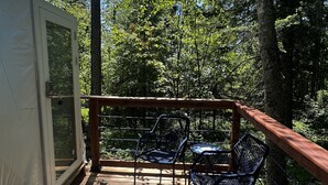 A wooden deck with two chairs and a table, surrounded by a wooden railing and a glass door leading to a room. -  Red Owl Retreat: The Peaks Geodesic Dome  (Bigfork)