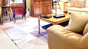 Una sala de estar con sofá, sillas, una mesa de centro, televisor y cortinas.