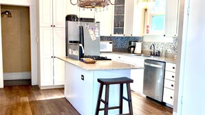Una cocina moderna con armarios blancos, una isla central con un taburete, electrodomésticos de acero inoxidable y una lámpara decorativa.