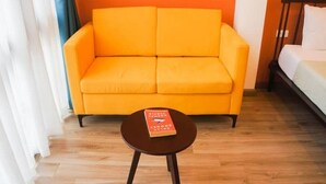 A room with a bright orange sofa, a small round table with a book, and a bed with white bedding.