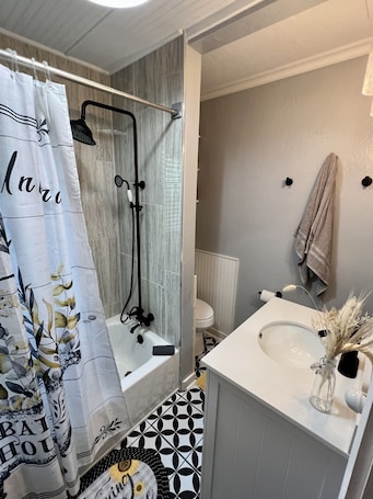 A bathroom with a shower, toilet, sink, and patterned floor tiles.