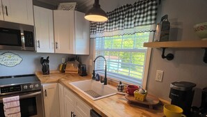 A kitchen with white cabinets, a stainless steel oven, a dishwasher, a sink, and a window with a checkered valance. - August special ✨99.00✨night!2B-2B cottage-hot tub-by Fall Creek Falls Park. (Spencer)