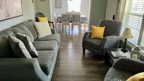 A living room with a grey sofa, a patterned armchair, and a houndstooth armchair with yellow cushions. A dining table with chairs is visible in the background. - August special ✨99.00✨night!2B-2B cottage-hot tub-by Fall Creek Falls Park. (Spencer)
