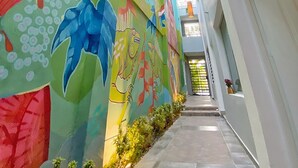 A narrow corridor with colorful murals on the walls, a tiled floor, and a ceiling with a grid pattern and hanging lights. - Green Oasis Hotel (La Romana)