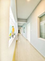Un couloir avec un mur de verre d’un côté, une porte de l’autre, et une fenêtre au fond.