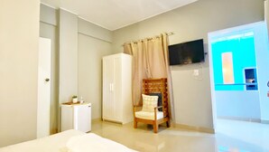 A hotel room with a bed, a chair, a wardrobe, a television, and a bathroom. - Green Oasis Hotel (La Romana)