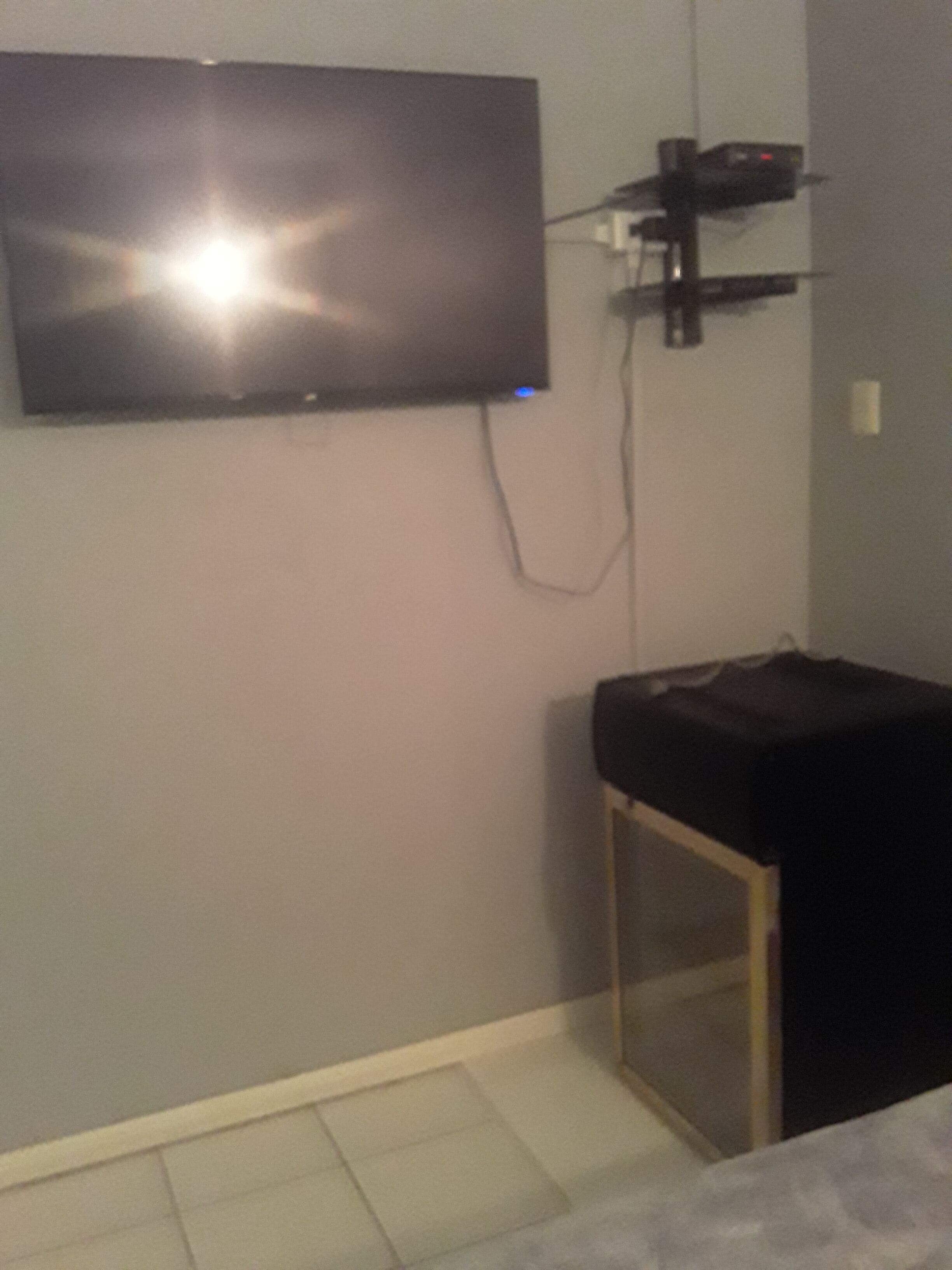 A room with a mounted television on the wall, a small table, and a cabinet.