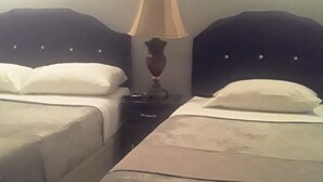Ein Hotelzimmer mit zwei Betten, einem Nachttisch mit Lampe und einem gefliesten Boden.