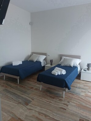 A hotel room with two beds, each with a blue bedspread and white pillows, and a small bedside table with a lamp. - Agriturismo Cutura Agri Resort (Parabita)