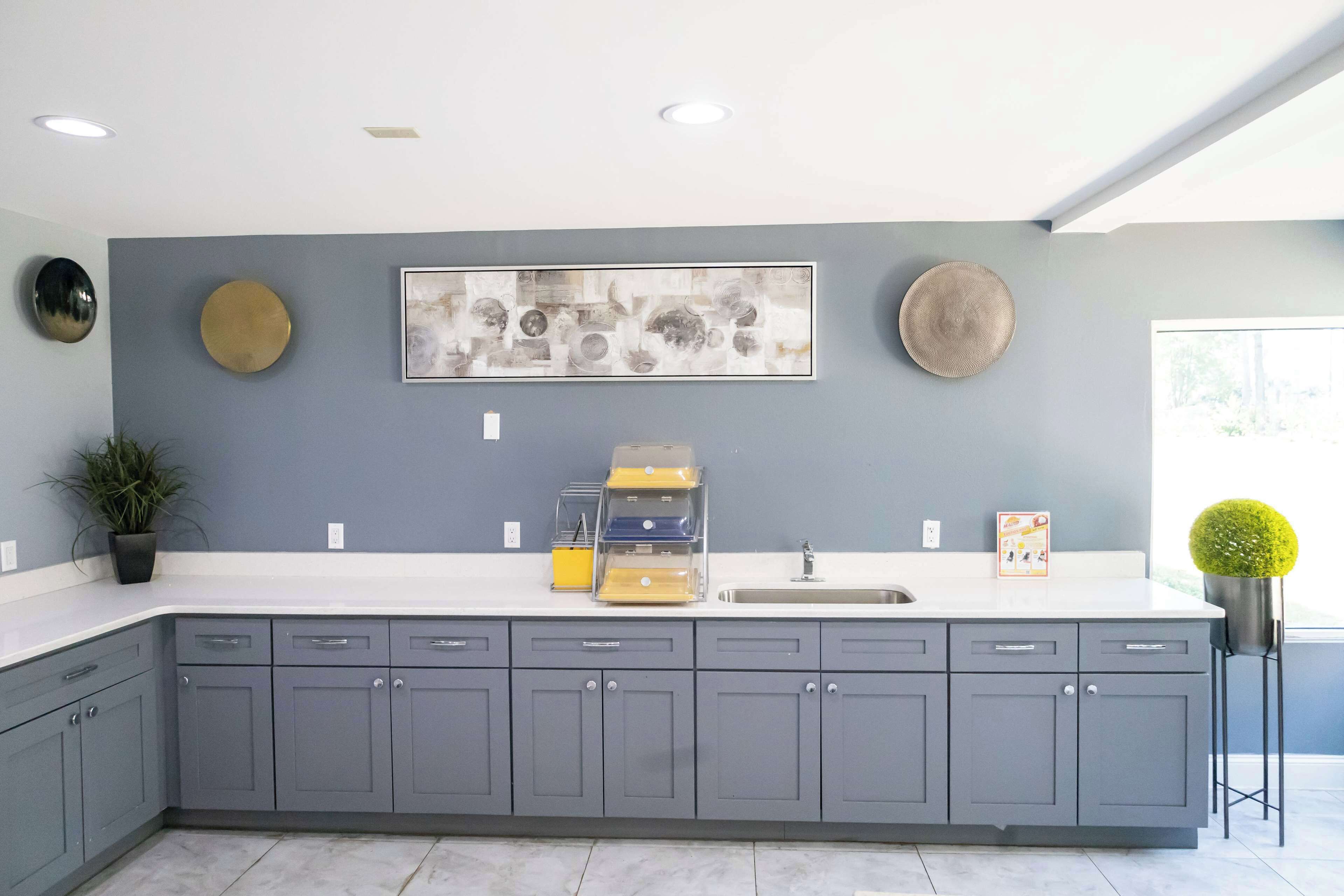 A modern kitchen with grey cabinets, a white countertop, and a large window providing natural light.