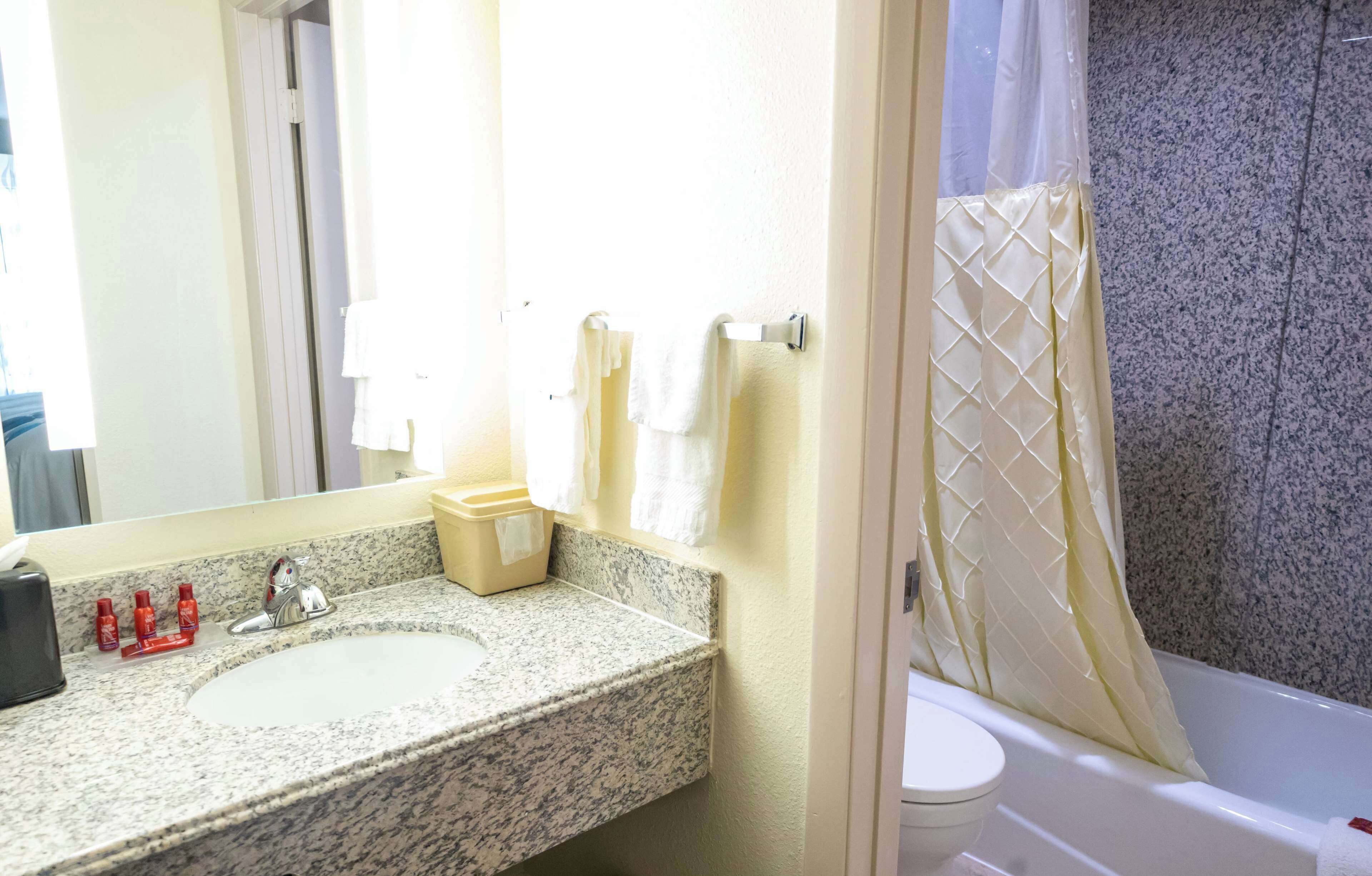 Un baño con lavamanos de granito, toallas blancas, inodoro y cortina de ducha.