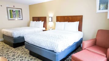 Habitación de hotel con dos camas, un sillón rojo y un suelo estampado.
