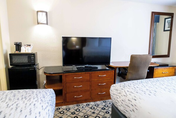 A hotel room with a bed, a desk with a flat-screen TV, a microwave, and a chair.