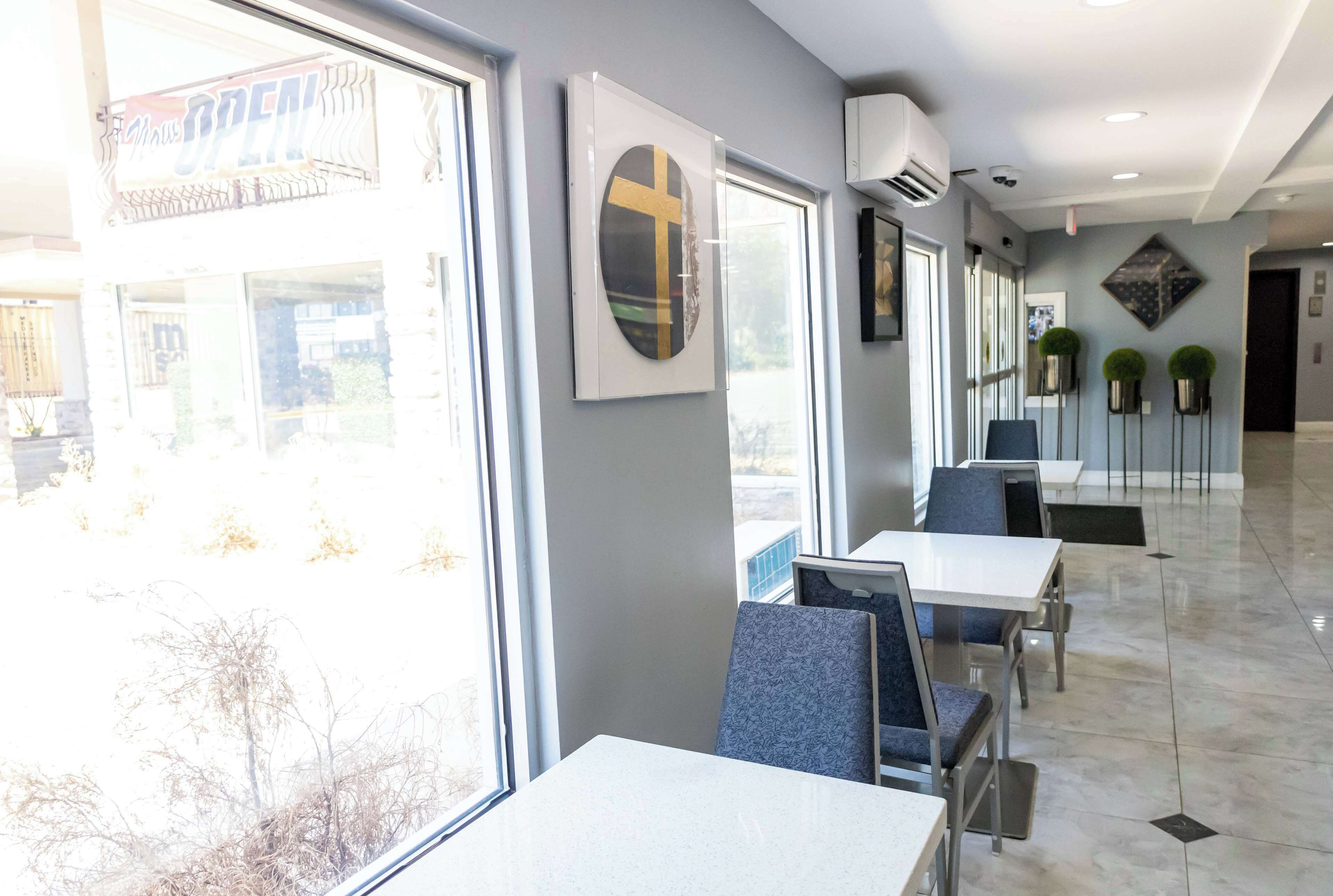 Un comedor luminoso y moderno con amplios ventanales, una obra de arte con forma de cruz y un piso de baldosas limpias.