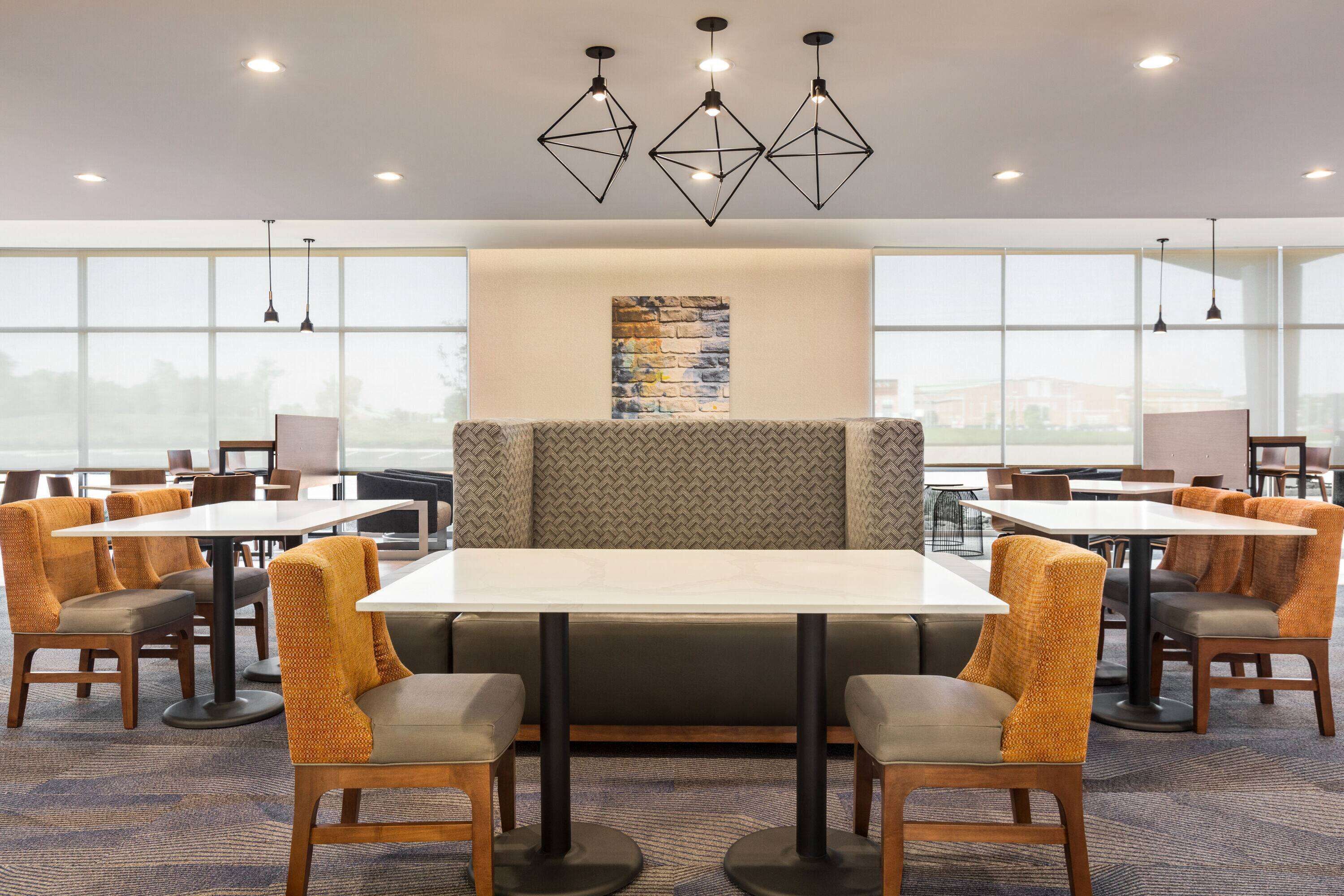 A modern dining area with high tables and chairs, a central seating area with a cushioned bench, and pendant lighting.