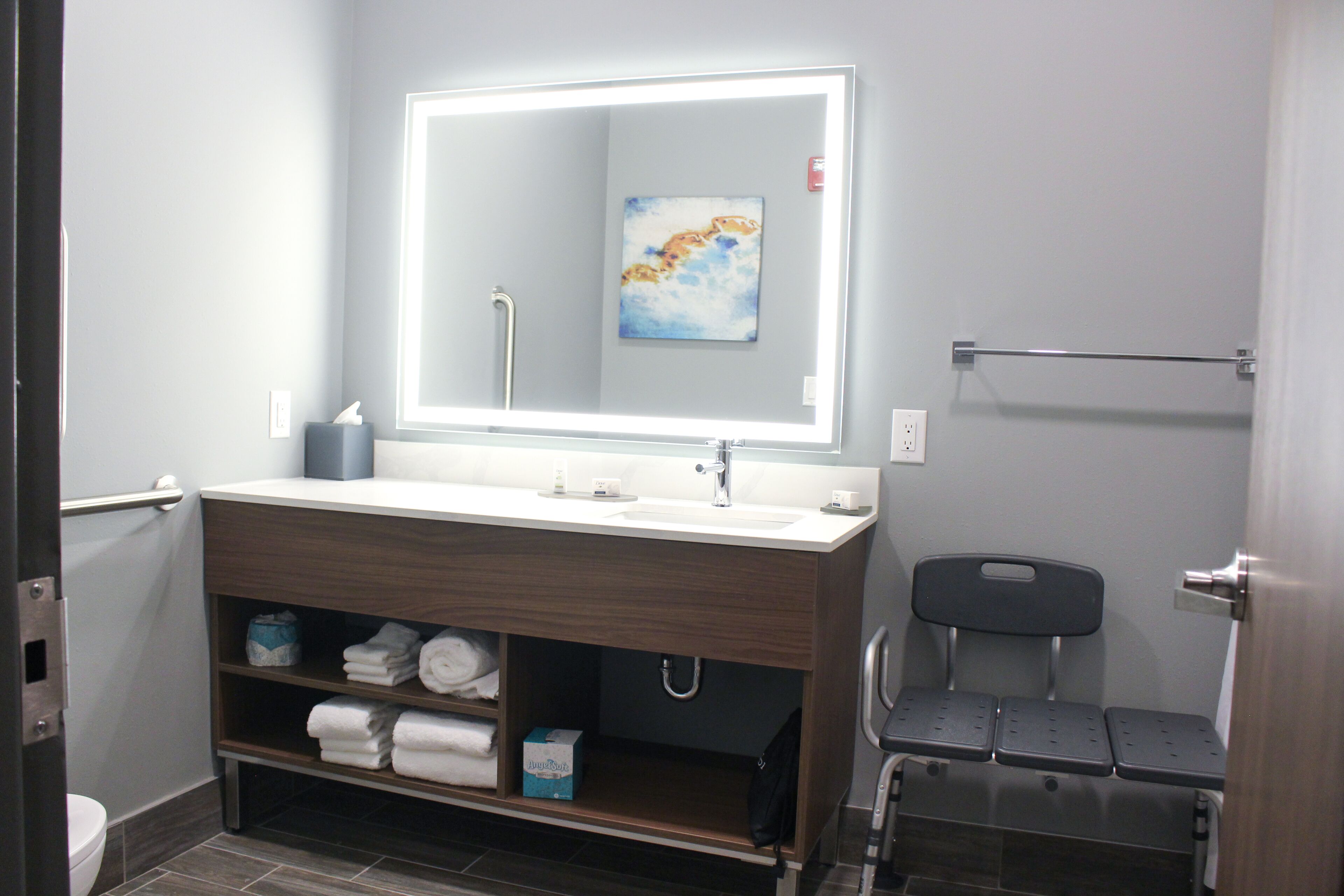 A modern bathroom with a large mirror, a sink, a towel rack, and a bench.