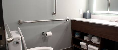 A modern bathroom with a white toilet, a handrail, a towel rack, and a mirror above the sink.
