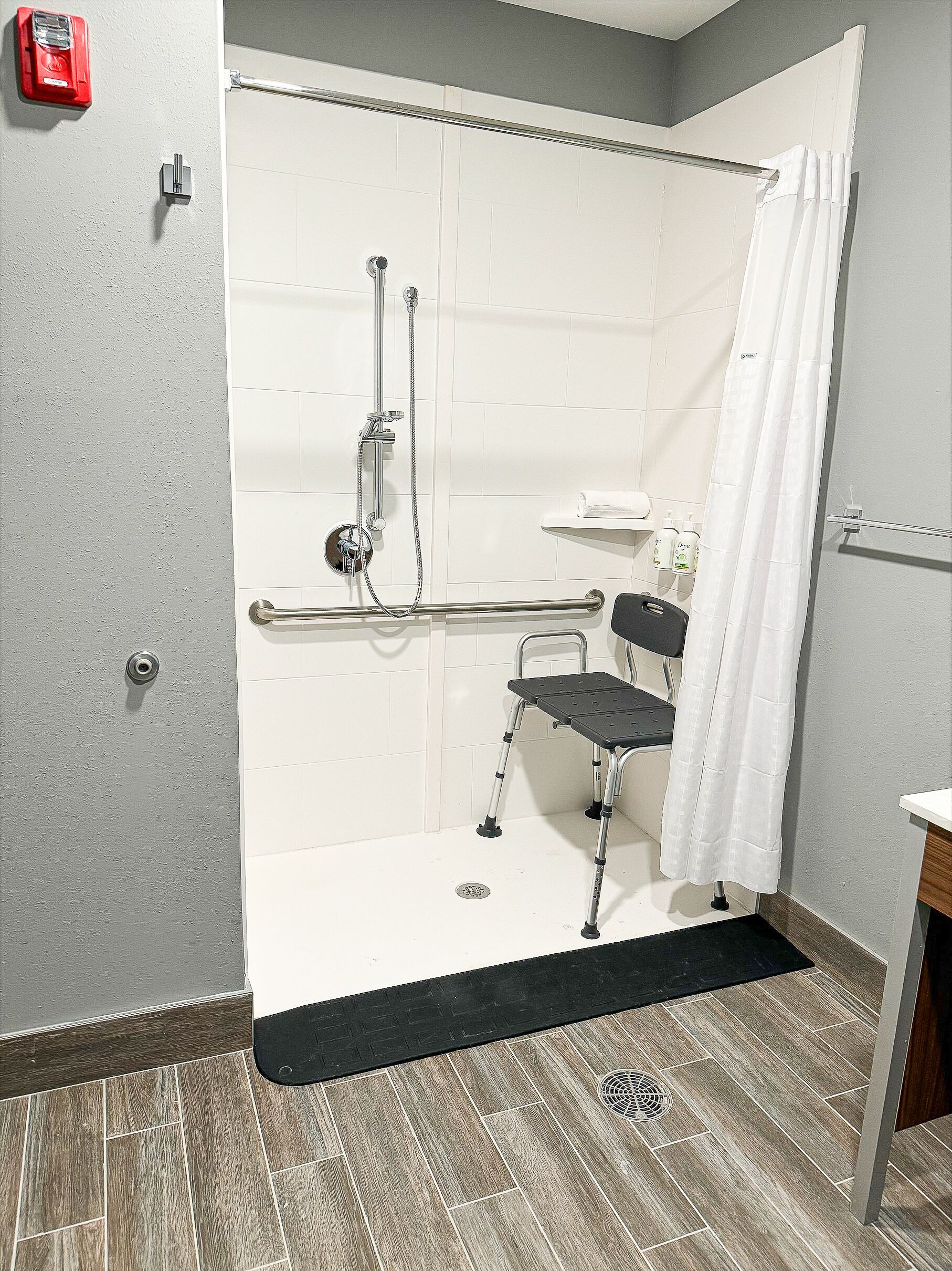 A shower area with a grab bar, a wheelchair, and a white shower curtain.