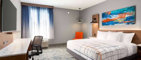 A modern hotel room with a large bed, a desk, and a chair. There is a painting on the wall and a window with curtains.