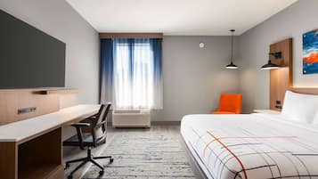 A hotel room with a bed, desk, chair, air conditioning unit, and a television.