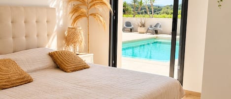 Ein Schlafzimmer mit einem großen Bett, Blick auf einen Swimmingpool und einem Balkon.