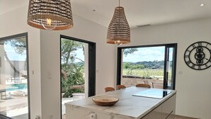 Une cuisine moderne dotée d’un îlot en marbre, de grandes fenêtres et offrant une vue sur l’extérieur.