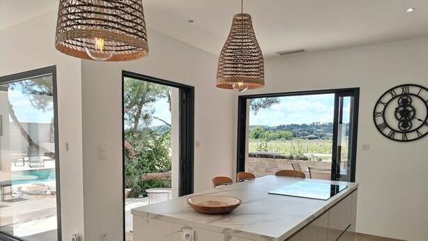 A modern kitchen with a marble island, large windows, and a view of the outdoors. - Air-conditioned villa, heated pool, vineyard view, calm setting (Pont-Saint-Esprit)