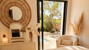 Une chambre à coucher comprenant un lit, une commode, un miroir et donnant sur une terrasse extérieure.