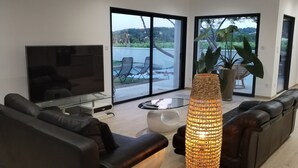 A modern living room with a sofa, a TV, a coffee table, and a large floor lamp. - Air-conditioned villa, heated pool, vineyard view, calm setting (Pont-Saint-Esprit)