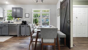 Cozinha moderna com armários cinza, área de refeições com mesa posta para quatro pessoas e uma grande janela com vista para o exterior.
